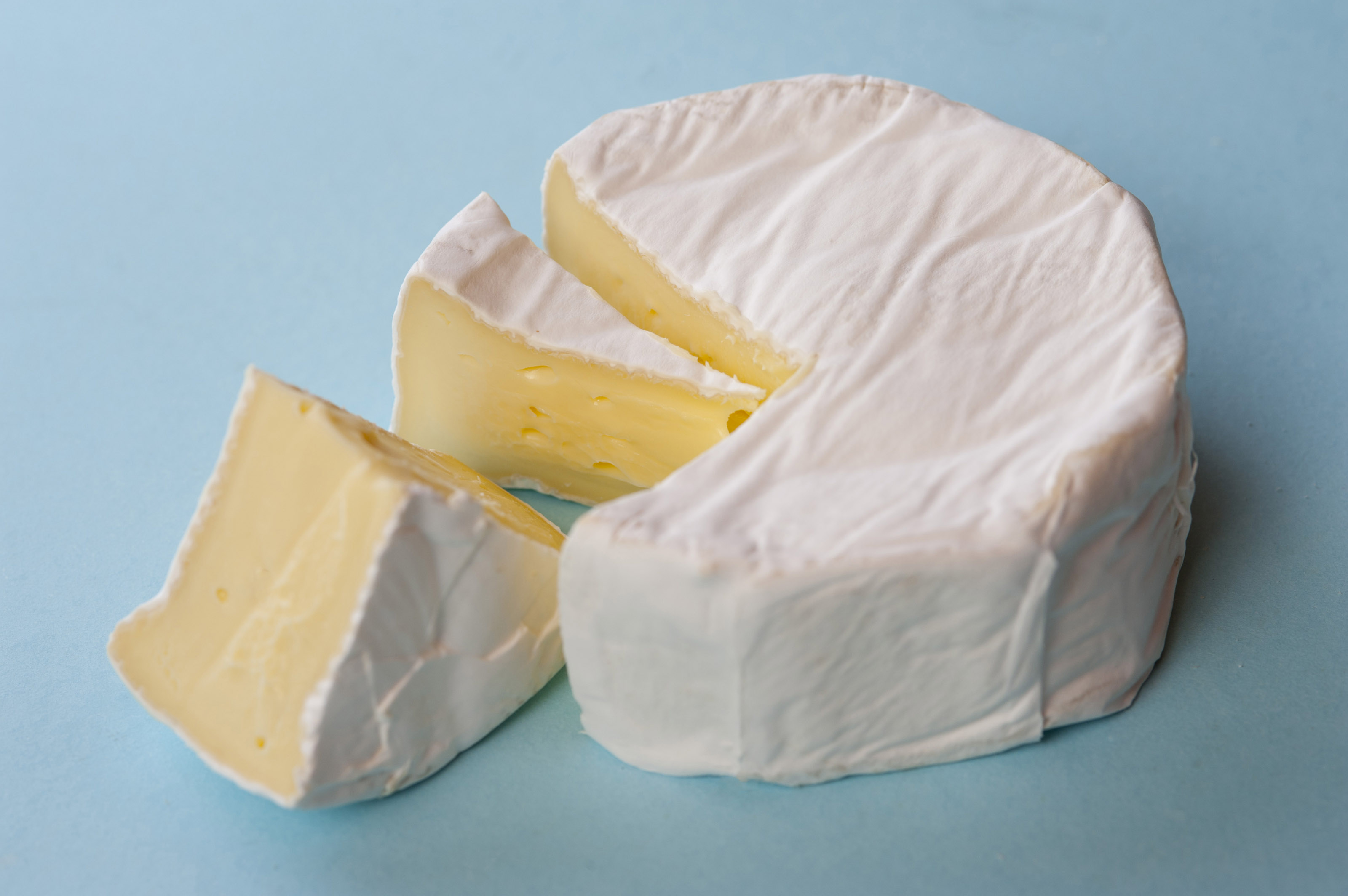 Round of mature soft brie cheese with two wedges removed to display the centre